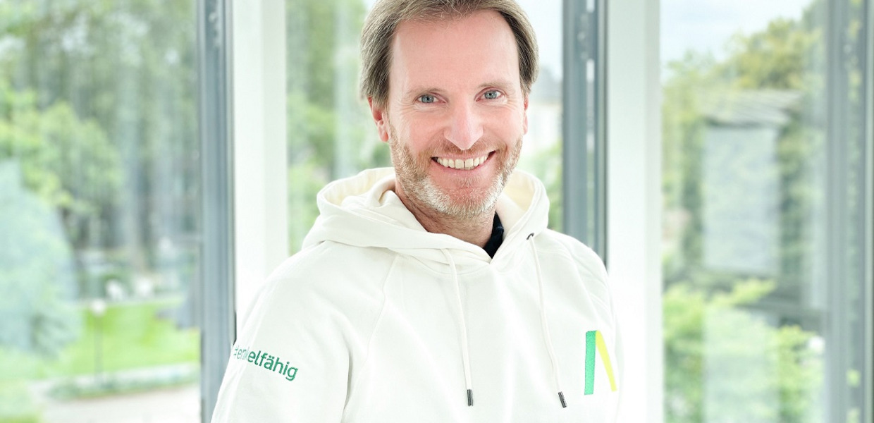 Mann im weißen Sweatshirt steht vor einem Fenster